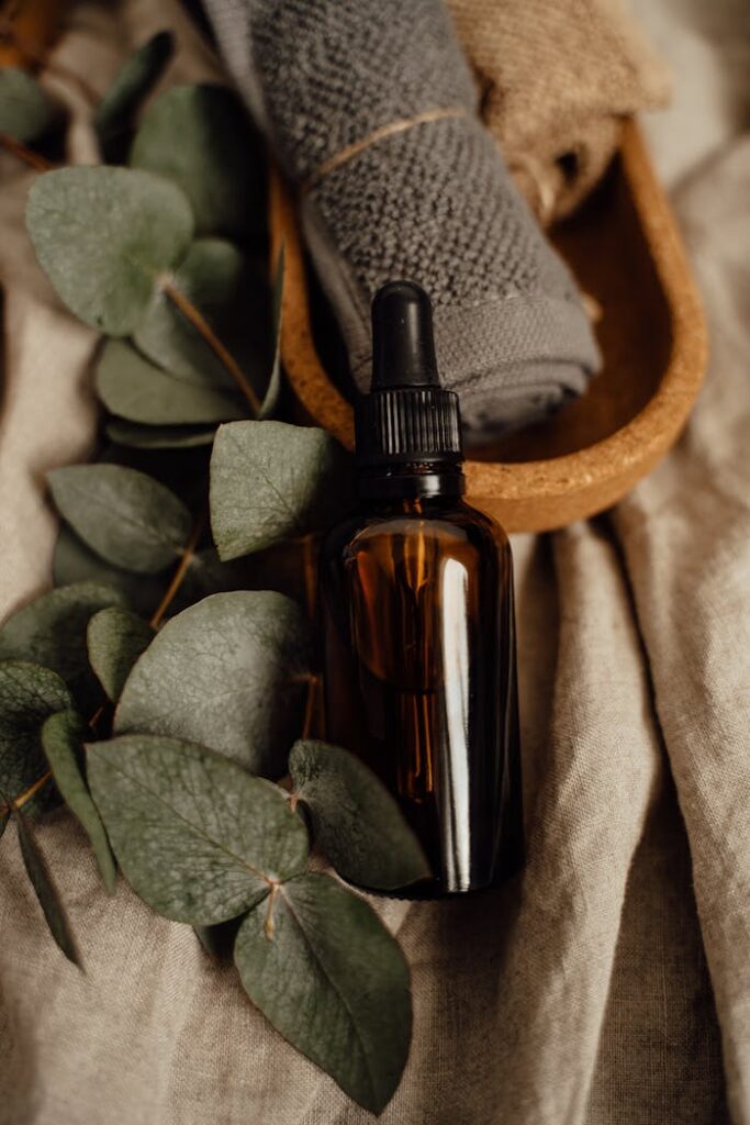 Amber glass skincare bottle on linen with eucalyptus and towels for a calming natural vibe.