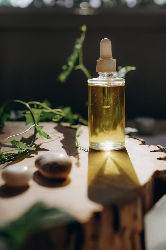 A clear bottle of aromatic oil on a wooden surface, surrounded by natural elements and sunlight.